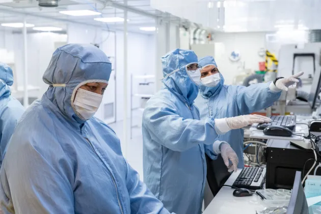 Photo of people in a cleanroom laboratory, wearing blue protective clothing.