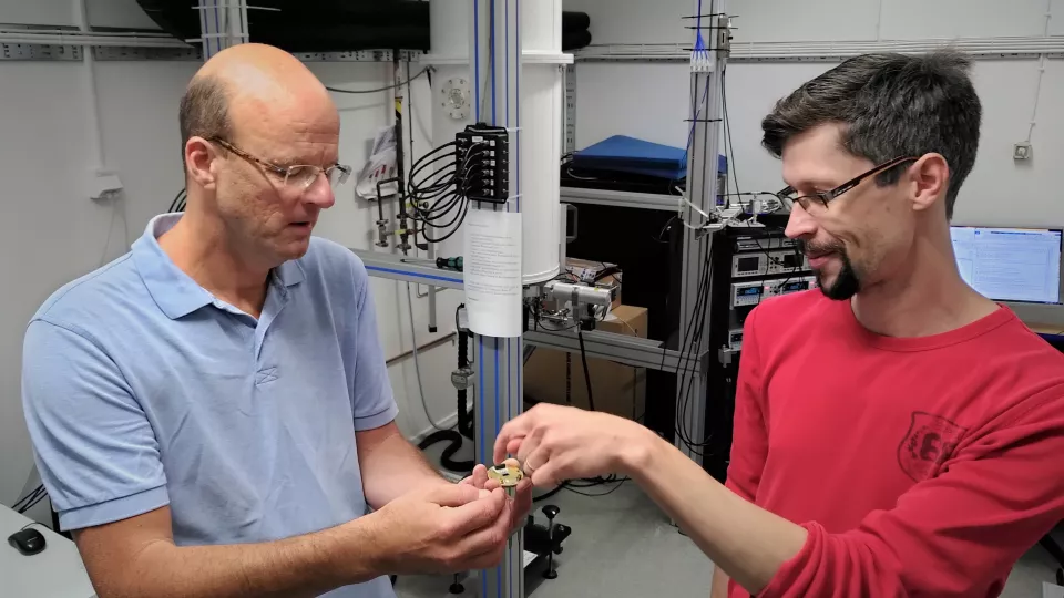 Photo of two researchers holding a brass component with microwave circuits.