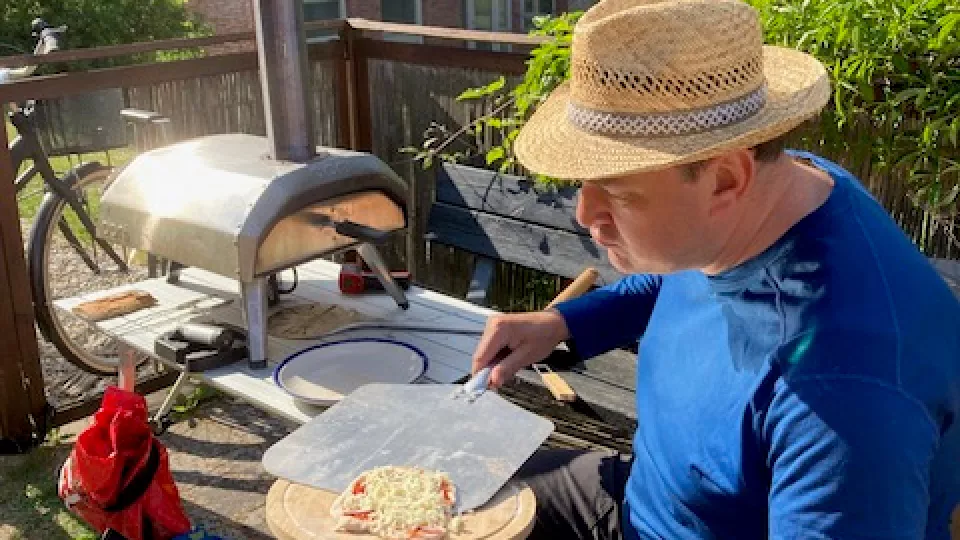 Man in straw hat puts pizza in table top oven