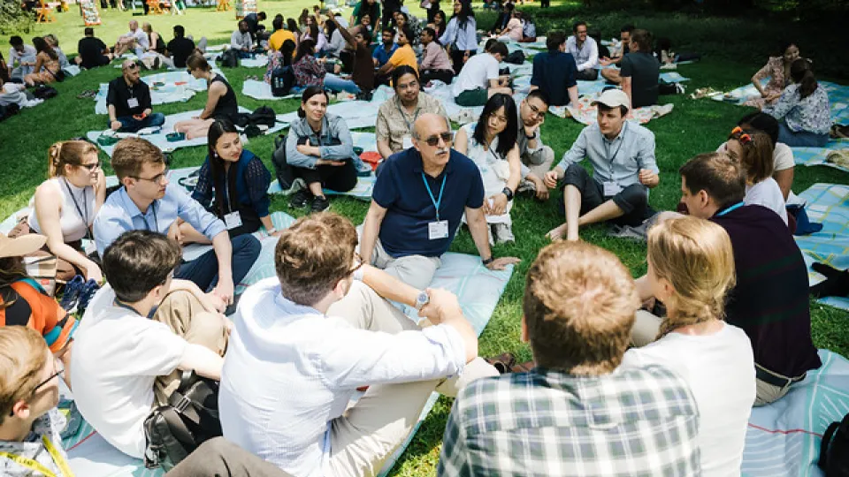 A large group of people wearing conference tags, sitting in the grass. Photo.