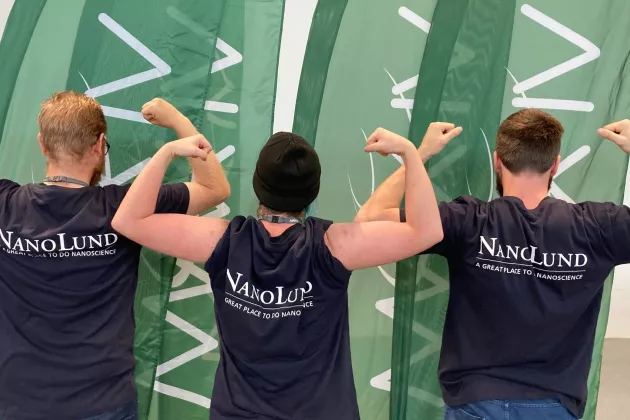 The backs of people showing off their muscles in t-shirts with the text ”NanoLund”.