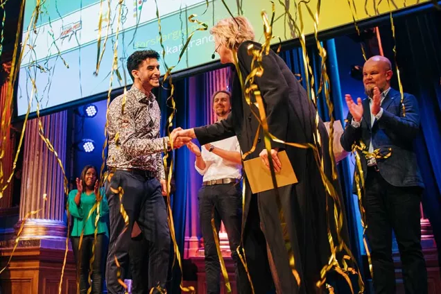 Photo of confetti on a person who’s just won a competition, being congratulated by others on a scene.