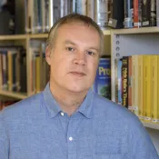 Photo of a man in front of a bookshelf.